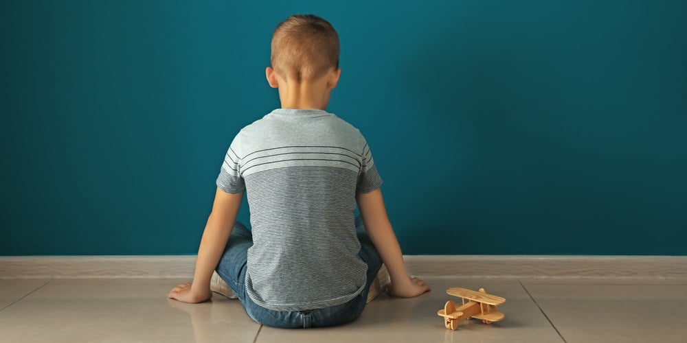 Little boy sitting near dark wall in empty room. Autism concept.